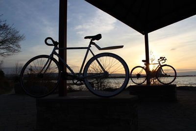 Bicycle on beach against sky during sunset