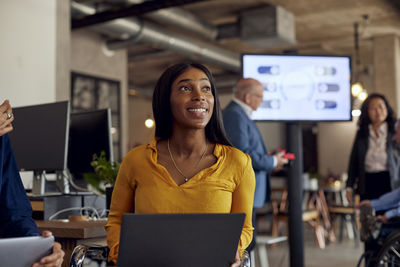 Smiling businesswoman sitting with laptop at creative office