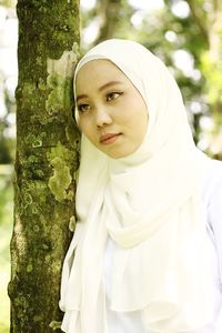 Portrait of young woman against tree trunk