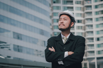 Male architecture looking away while standing against building