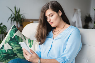 Young woman looking away while sitting on sofa at home