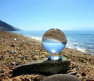 Close-up of crystal ball on sand at beach against clear blue sky