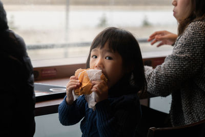 Portrait of cute girl eating fast food with mother