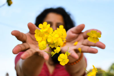 Midsection of woman holding yellow flowering plant against sky