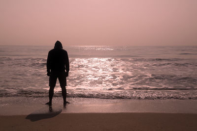 Rear view of men on beach against sky during sunset