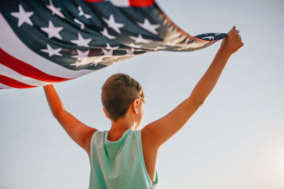 Rear view of boy holding american flag against clear sky