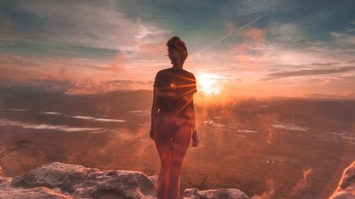 Rear view of woman standing on mountain against cloudy sky during sunset