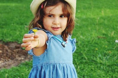Portrait of cute girl holding flower while standing on field