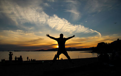 Silhouette of man with arms outstretched standing on lake during sunset