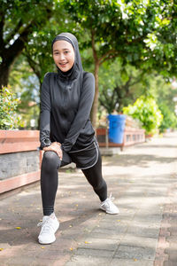 Full length portrait of smiling young woman standing on footpath