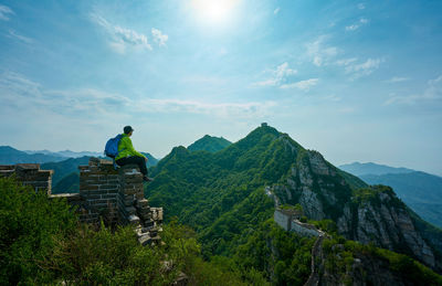 Man sitting on great wall of china by mountains against sky