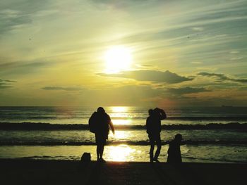 Silhouette people on beach against sky during sunset