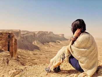 Woman sitting on land against clear sky