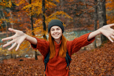 Portrait of young woman with arms raised standing during autumn