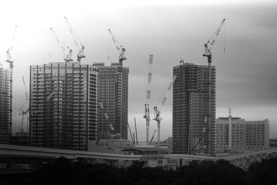 Cranes and buildings against sky in city