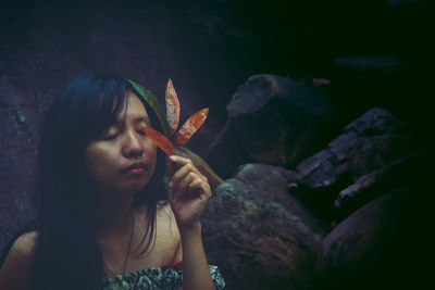 Woman with eyes closed holding leaves against rocks