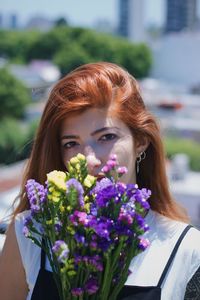 Portrait of young woman with purple flowers against blurred background