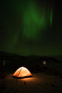 Illuminated tent at beach against sky at night