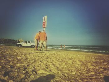 Rear view of people on beach against clear sky