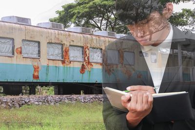 Double exposure image of businessman writing in diary and rusty train