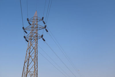 Low angle view of electricity pylon against clear blue sky