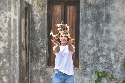 Portrait of smiling woman throwing leaves while standing against wall