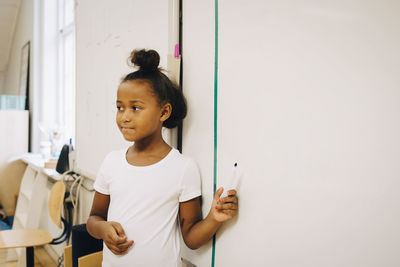 Schoolgirl showing spelling on whiteboard at classroom