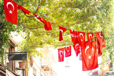 Low angle view of red flags hanging on tree against building