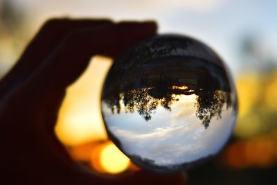 Close-up of hand holding glass against sky during sunset