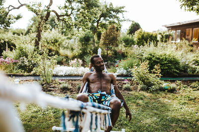 Shirtless man relaxing on hammock in yard