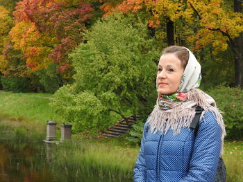 Woman looking away while standing by lake against plants