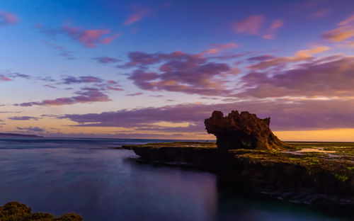 Rock formation on beach against sky during sunset