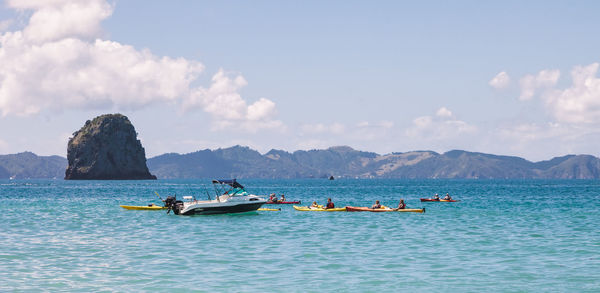 People kayaking in sea against sky