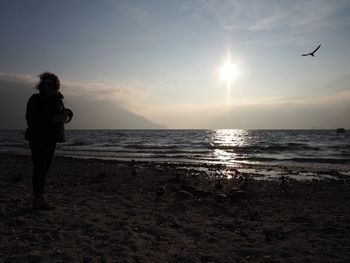 Silhouette man photographing sea against sky during sunset