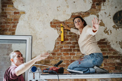 Couple discussing while measuring brick wall during home renovation