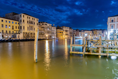 Boats moored in canal against illuminated buildings in city at night