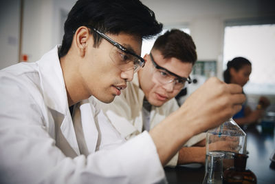 Young male students mixing solutions in glassware at chemistry laboratory