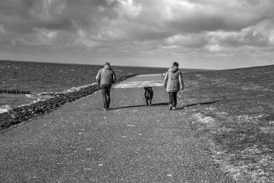 Rear view of people walking on sea shore against sky