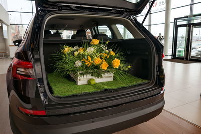 A basket of flowers is in the open trunk of a car on the territory of a car dealership.