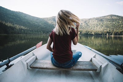 Rear view of woman sitting on boat against lake