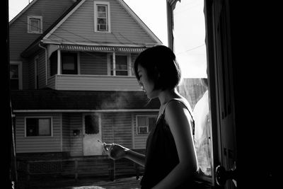 Side view of young woman smoking while standing in balcony