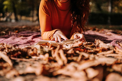 Midsection of woman with autumn leaves on field