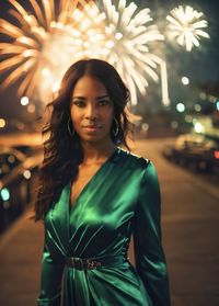 Portrait of young woman standing against illuminated string lights at night