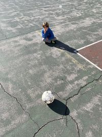 High angle view of boy with ball sitting in court