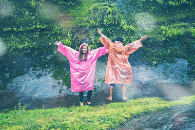 Full length of couple wearing raincoat standing in forest during rainy season