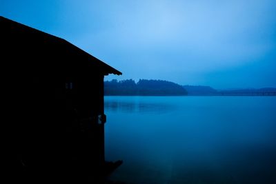 Scenic view of lake by silhouette buildings against blue sky