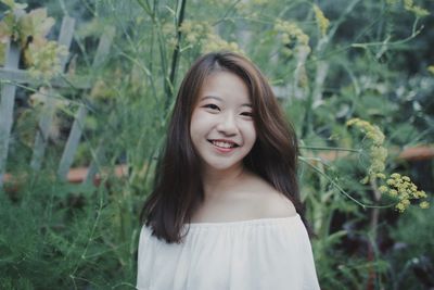 Portrait of smiling young woman by plants at public park