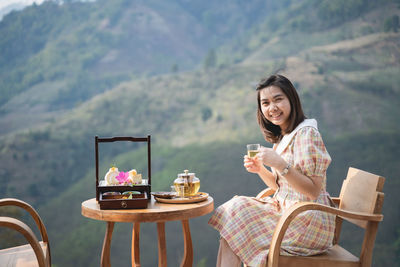 Young woman sitting on chair at table against mountain