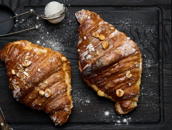 Baked croissant on a wooden board and sprinkled with powdered sugar, black table. appetizing 