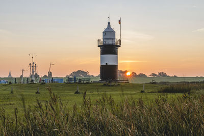 Lighthouse on field against sky during sunset